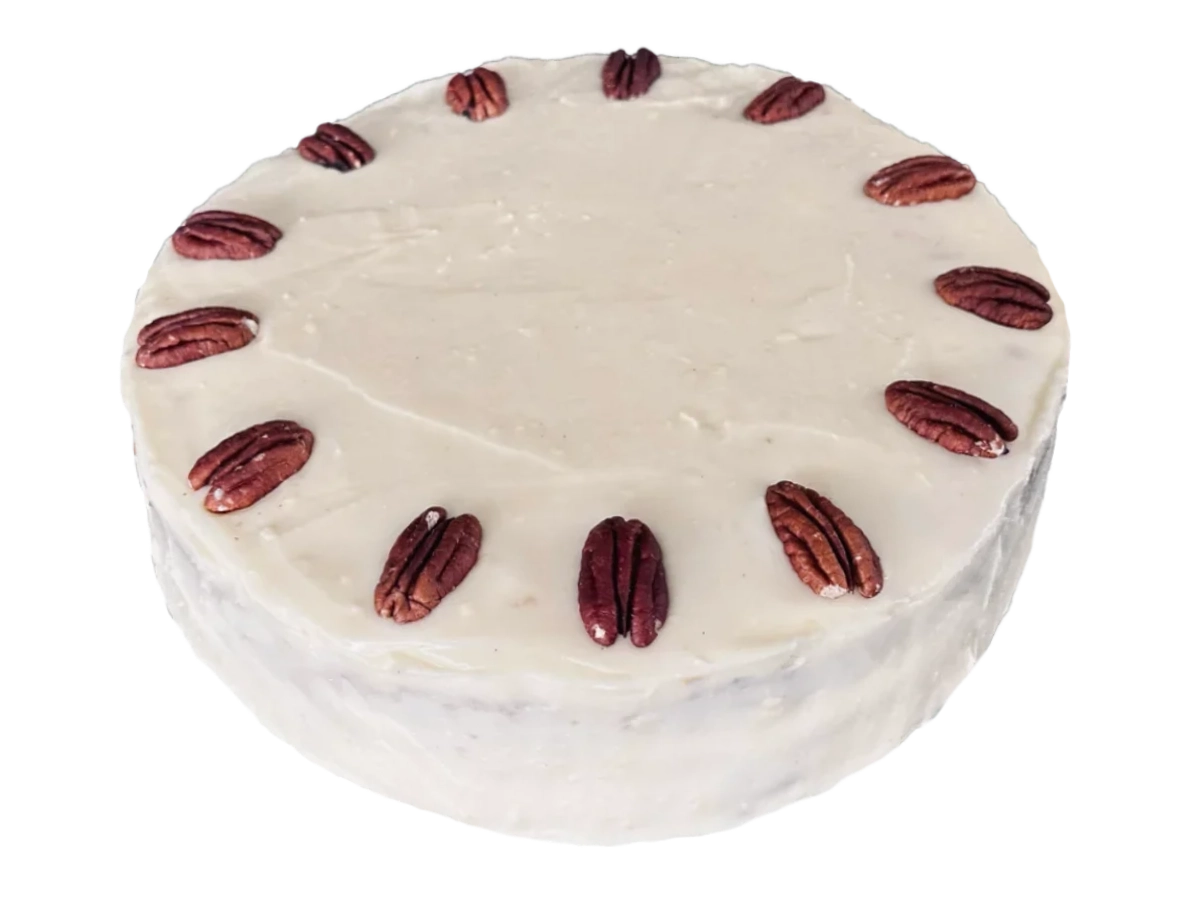 Hummingbird cake with pale cream cheese frosting and a ring of pecan halves on top.
