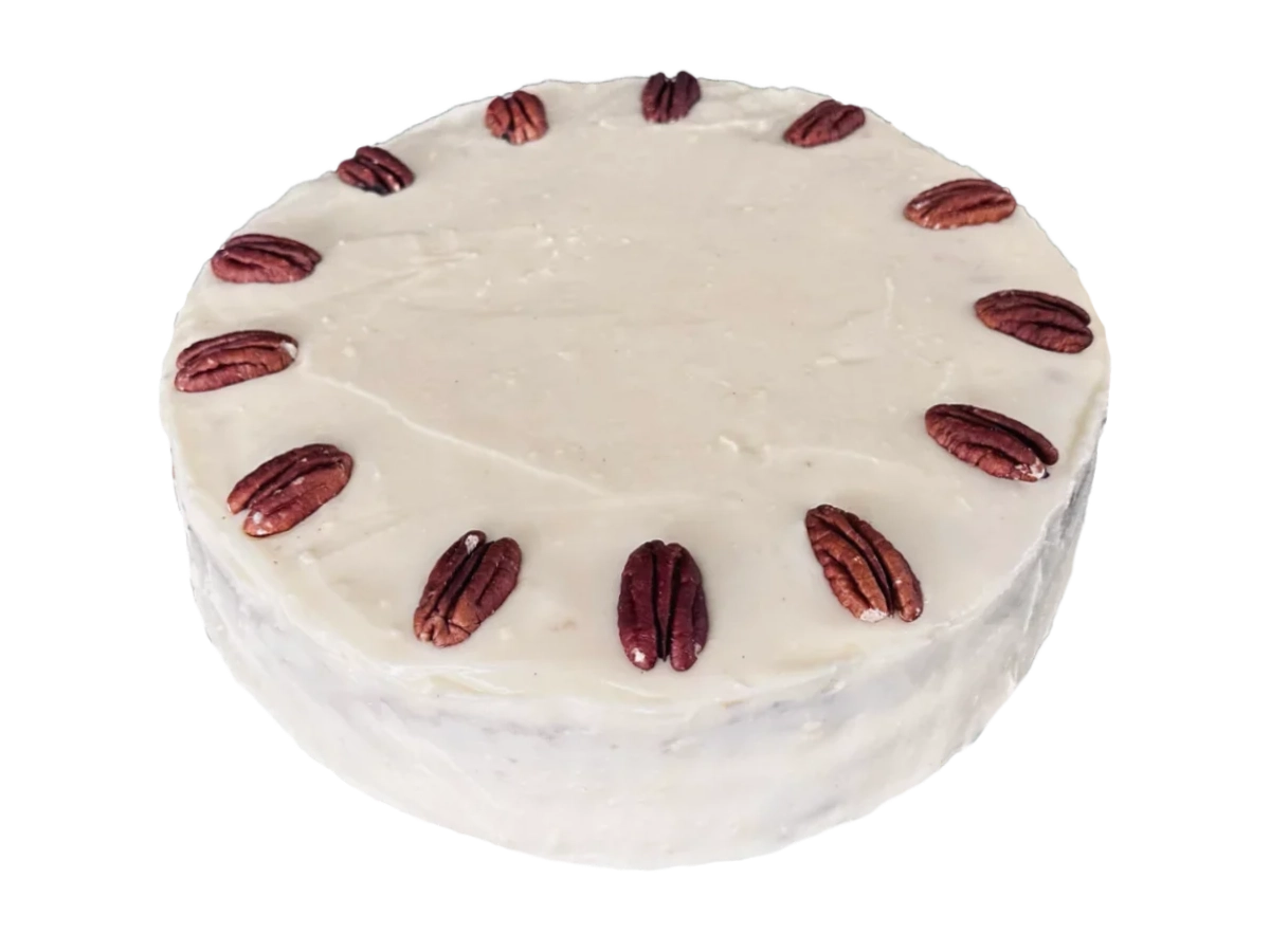 Hummingbird cake with pale cream cheese frosting and a ring of pecan halves on top.